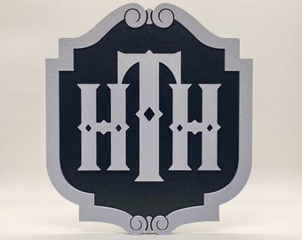 May include: A grey and black wooden sign with the letters "HTH" in a stylised font. The sign is shaped like a shield with a decorative border.