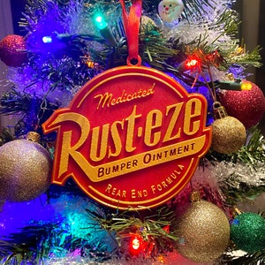 May include: A red and gold Christmas ornament shaped like a round sign with the words "Medicated Rust-eze Bumper Ointment Rear End Formula" on it.
