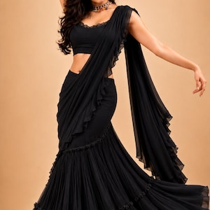Puede incluir: Un sari negro que presenta una blusa sin mangas con un escote adornado con encaje. La falda est&aacute; muy plisada con un dise&ntilde;o escalonado y peque&ntilde;os detalles florales en las costuras. Un pallu largo y fluido con bordes con volantes.