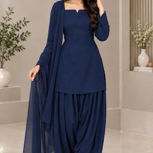 Könnte beinhalten: Ein einfarbiges marineblaues Salwar-Kameez-Set, bestehend aus einer langärmeligen Tunika mit quadratischem Ausschnitt und kleiner Kerbe, kombiniert mit einer plissierten Salwar-Hose und einem passenden, leichten, transparenten Dupatta.