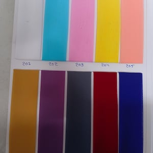 May include: A color swatch card featuring ten vertical strips of fabric in white, turquoise, pink, yellow, peach, mustard, purple, dark gray, red, and blue. Each strip is labeled with a handwritten number from 201 to 210 below the color sample.