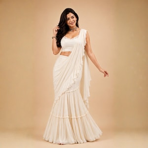 May include: A cream-coloured two-piece ensemble consisting of a sleeveless crop top and a floor-length skirt with a draped, ruffled overlay. The skirt features a tiered design with delicate pleats and a subtle, flowing silhouette in a solid light hue.