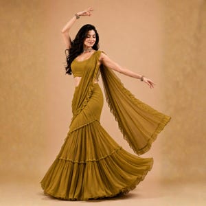 May include: A mustard yellow saree featuring a sleeveless blouse and a long, pleated skirt with ruffled edges. The garment includes a matching draped pallu that extends from the shoulder, creating a layered, flowing silhouette with consistent colour.