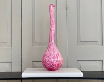 May include: A tall, pink glass vase with a swirling, textured design. The vase has a bulbous base and a long, slender neck.