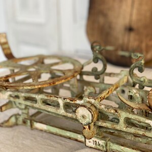 Pu&ograve; includere: Una bilancia vintage in metallo verde con una ruota arrugginita e dettagli decorativi. La bilancia ha una superficie verniciata di bianco con alcuni scheggiamenti ed &egrave; etichettata "10L".