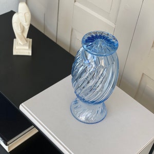 May include: A light blue glass vase with a swirl design. The vase has a round base and a wide opening.