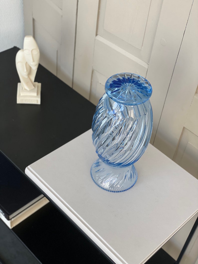 May include: A light blue glass vase with a swirl design. The vase has a round base and a wide opening.