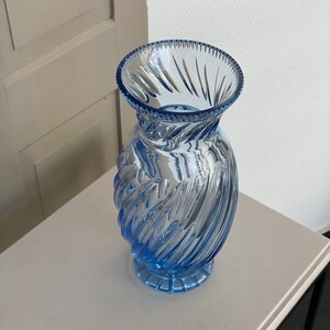 May include: A light blue glass vase with a swirl design. The vase has a wide mouth and a narrow base.