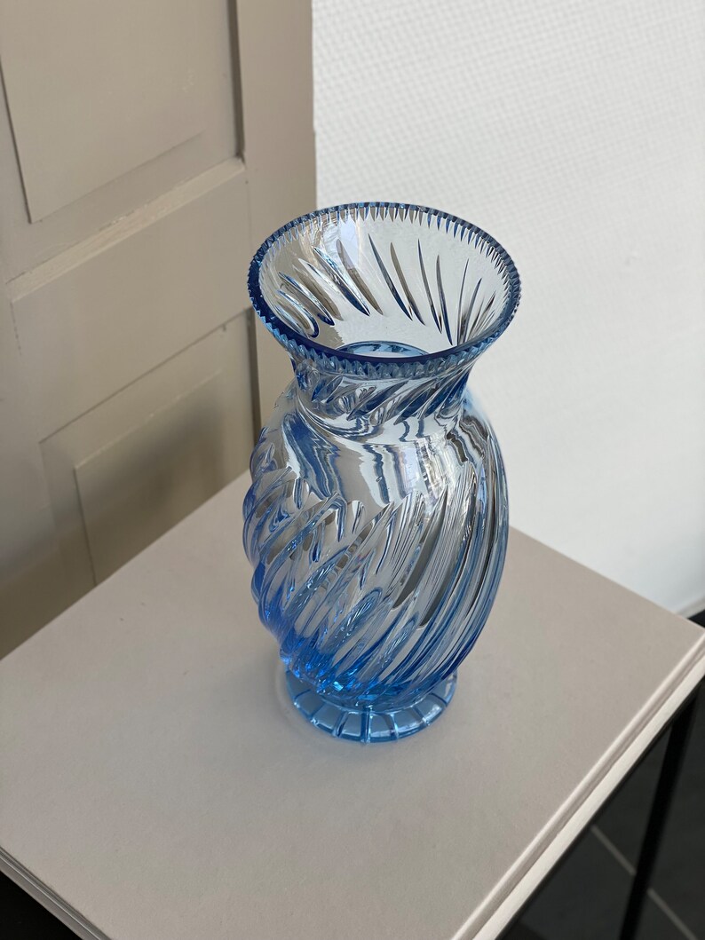 May include: A light blue glass vase with a swirl design. The vase has a wide mouth and a narrow base.