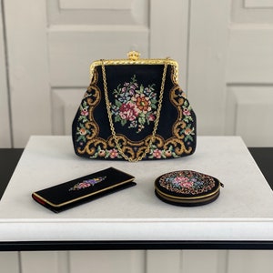 Pode incluir: Uma bolsa preta bordada com fecho e corrente dourados, uma carteira preta bordada e um compacto redondo preto bordado.