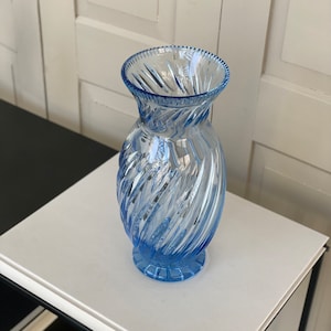 May include: A blue glass vase with a swirl design. The vase is clear and has a textured surface.