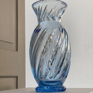 May include: A light blue glass vase with a swirl design. The vase has a wide mouth and a narrow base.