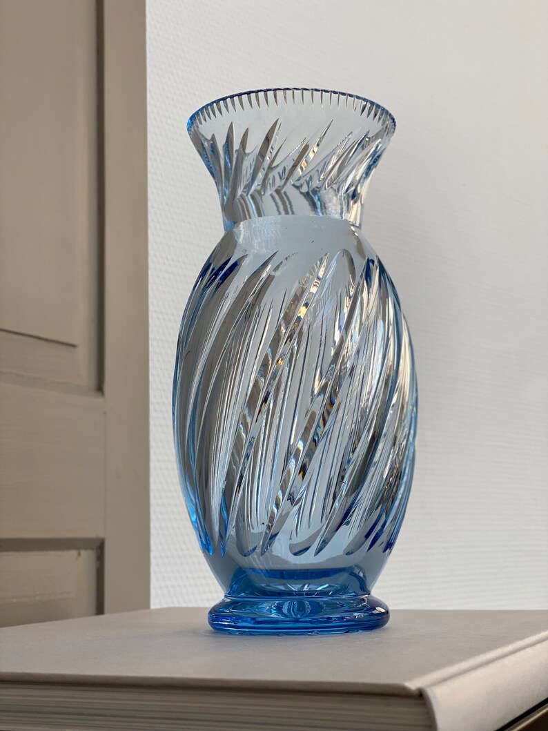 May include: A light blue glass vase with a swirl design. The vase has a wide mouth and a narrow base.