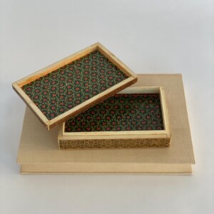May include: A small wooden box with a floral pattern inside. The box is open and the lid is resting on top of a book.