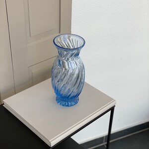 May include: A light blue glass vase with a swirl design. The vase is sitting on a white surface.