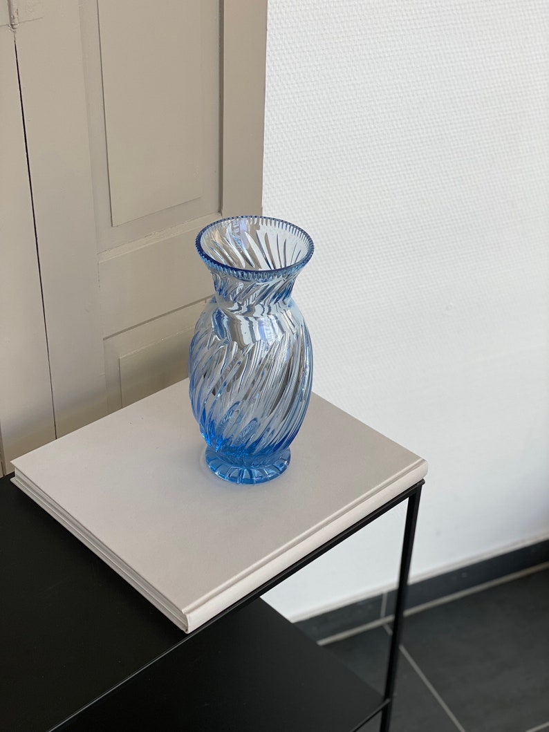 May include: A light blue glass vase with a swirl design. The vase is sitting on a white surface.