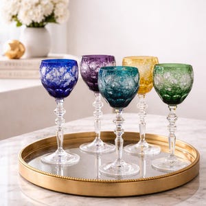 Könnte beinhalten: Sechs farbige Weingläser mit aufwendigen floralen Mustern. Die Gläser sind in Blau, Lila, Türkis, Gelb und Grün gehalten und stehen auf einem goldfarbenen Tablett. Die Stiele sind klar und detailliert.
