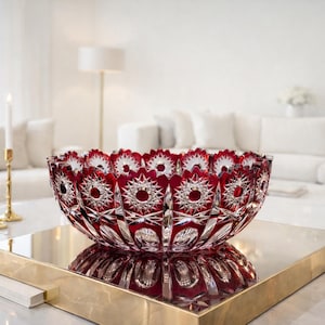 Può includere: Una grande ciotola di cristallo rosso rubino con un motivo a stella. La ciotola è appoggiata su un vassoio dorato, che riflette il suo design intricato. È un pezzo decorativo, perfetto per un soggiorno o una sala da pranzo.