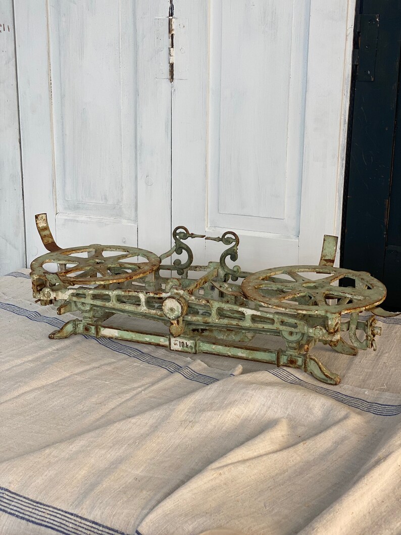 Pu&ograve; includere: Una bilancia vintage in ghisa verde con due piattaforme circolari e una leva centrale. La bilancia presenta dettagli intricati ed &egrave; contrassegnata dal numero "181".