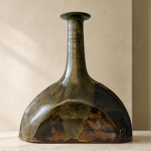 Könnte beinhalten: Eine Keramikvase mit breitem, flachem Boden und einem hohen, schlanken Hals. Die Oberfläche ist mit einer gesprenkelten Glasur in Dunkelgrün, Braun und Schwarz versehen und hat ein glattes, reflektierendes Finish. Der Text AI MODIFIED ist unten rechts sichtbar.