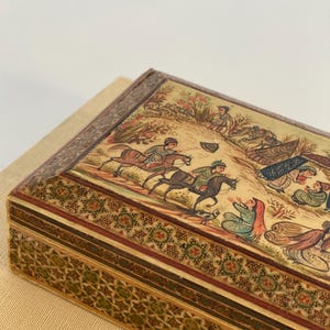 May include: A rectangular wooden box with intricate inlaid designs in shades of brown, green, and gold. The top of the box features a hand-painted scene depicting people on horseback and figures in a landscape.