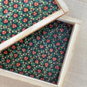 May include: Two square wooden trays with a geometric pattern of green, red, and black triangles. The trays are nested together.