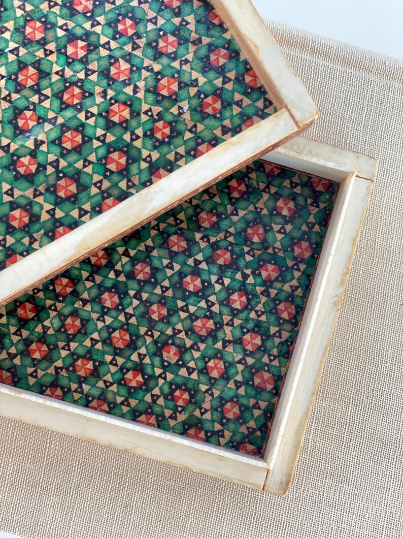 May include: Two square wooden trays with a geometric pattern of green, red, and black triangles. The trays are nested together.