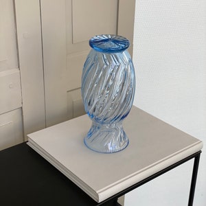 May include: A light blue glass vase with a swirl design. The vase is sitting on a white surface.