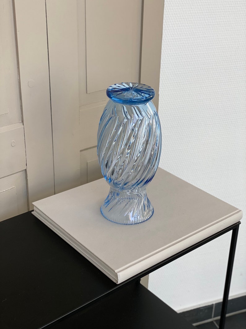 May include: A light blue glass vase with a swirl design. The vase is sitting on a white surface.