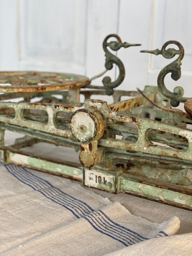 Pu&ograve; includere: Bilancia antica in ghisa verde con accenti in metallo decorativi e un quadrante bianco. La bilancia &egrave; appoggiata su un tessuto a strisce bianche e blu.