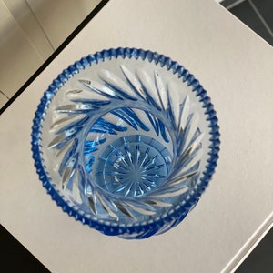 May include: A clear glass vase with a blue tint and a cut glass design. The vase has a round base and a wide opening.