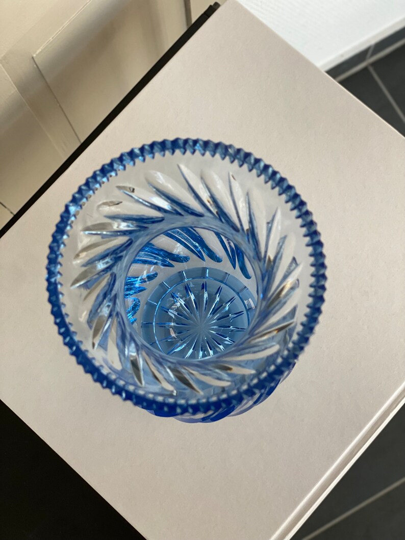 May include: A clear glass vase with a blue tint and a cut glass design. The vase has a round base and a wide opening.