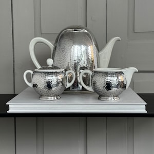 May include: A silver tea set with a hammered finish. The set includes a teapot, creamer, and sugar bowl.