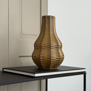 May include: A brown ceramic vase with a textured, ribbed design sits on a black table with a book on top. The vase has a rounded, bulbous shape and a narrow neck.