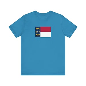 Op de afbeelding: Een lichtblauw T-shirt met een witte en rode vlag van de staat North Carolina, gedrukt op de voorkant.