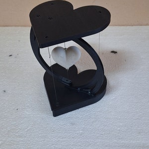 May include: A black heart-shaped stand with a white heart suspended inside. The stand is made of wood and has a smooth finish.