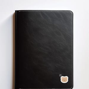 May include: A black leather-bound journal with a small brown bear sticker on the bottom right corner.