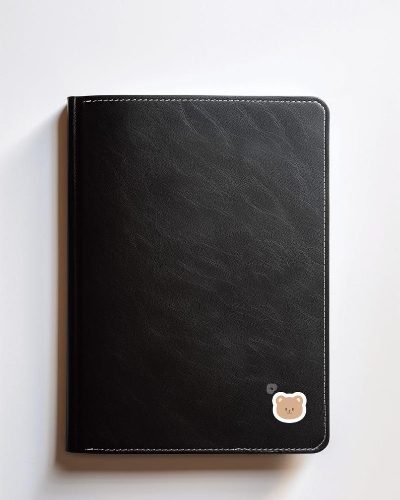 May include: A black leather-bound journal with a small brown bear sticker on the bottom right corner.