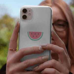 May include: A clear phone case with a watermelon design. The watermelon is pink with black seeds and a green rind.