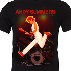 May include: Black t-shirt with a photo of Andy Summers, a musician, playing a guitar on stage. The text "ANDY SUMMERS" is printed in red on the shirt.