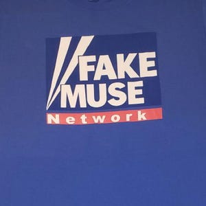 Könnte beinhalten: Ein blaues T-Shirt mit dem Aufdruck "FAKE MUSE Network" in Weiß und Rot. Das Design hat eine quadratische Form mit weißen diagonalen Linien.