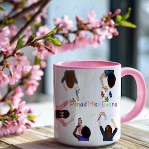 May include: White ceramic mug with a pink handle and rim, featuring colorful illustrations of children and the text "Panad Miss Evans." The mug is decorated with drawings of children holding toys and a rainbow.