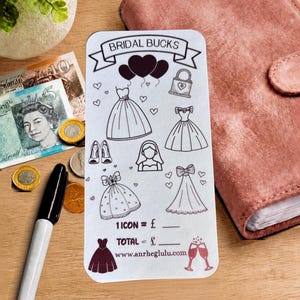Peut inclure: Une carte rectangulaire blanche intitulée BRIDAL BUCKS avec des illustrations au trait noir de robes de mariée, cœurs, ballons, sac à main, chaussures et voile. La carte inclut des champs pour 1 ICON = £ et TOTAL = £, et le site www.anrheglulu.com.