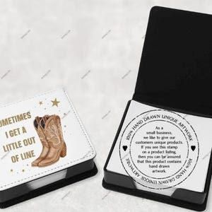 Può includere: Blocco note bianco con base nera e un design dorato con un paio di stivali da cowboy marroni e il testo "Sometimes I get a little out of line". Il blocco note ha un retro nero con un adesivo bianco che dice "100% Hand Drawn Unique Artwork" con una breve descrizione testuale dell'opera d'arte.