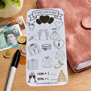 Peut inclure: Une carte de suivi d'épargne rectangulaire blanche intitulée FOREVER FUND avec des illustrations au trait noir d'icônes de mariage incluant des cœurs, une robe, un costume, des bagues et un gâteau. La carte affiche 1 ICON = £ et TOTAL = £ et anrheglulu.com.