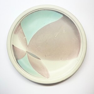 May include: A white ceramic plate with a raised rim and a design of overlapping pastel pink and blue shapes.