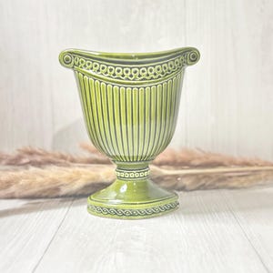 May include: A green ceramic vase with a fluted design and a decorative rim. The vase has a wide base and a narrow neck.