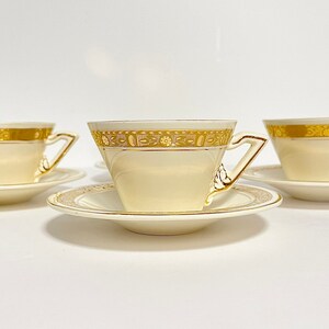 May include: Three white teacups with gold trim and matching saucers. The cups and saucers have a delicate floral pattern in gold.