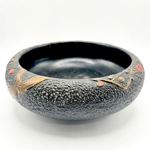 May include: A black ceramic bowl with a textured surface and gold and red accents. The bowl has a wide rim and a rounded bottom.