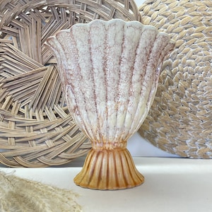 May include: A white ceramic vase with a scalloped rim and a textured, aged finish. The vase has a wide, round base and a narrow neck. The vase is a light beige color with brown accents.